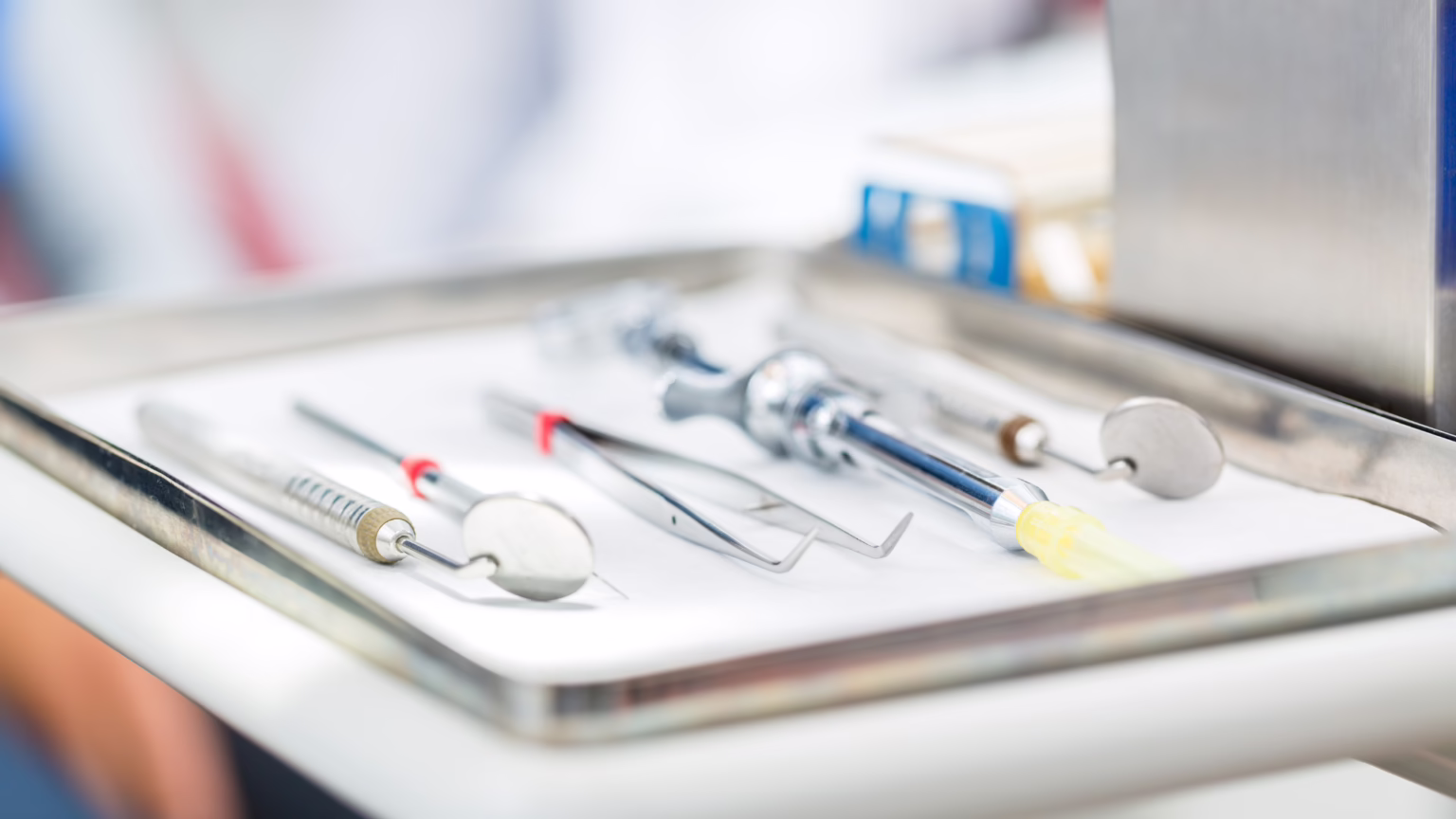 Dental tools laid out on a sterile metal tray in a dental clinic setting.
